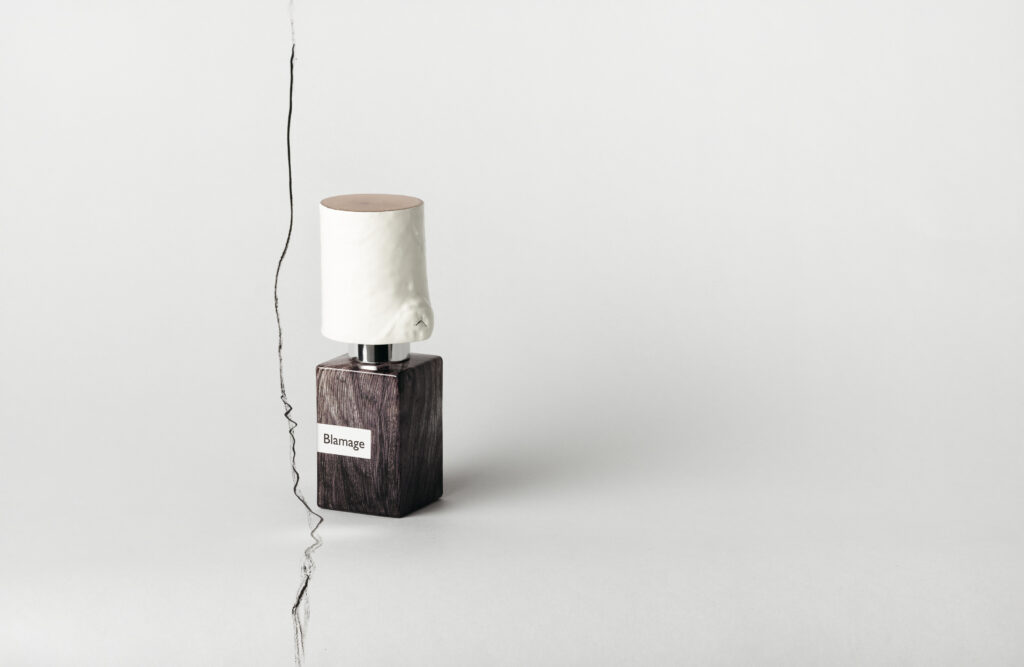 Nasomatto Blamage perfume bottle positioned close to an irregular vertical line against a minimalist light background.