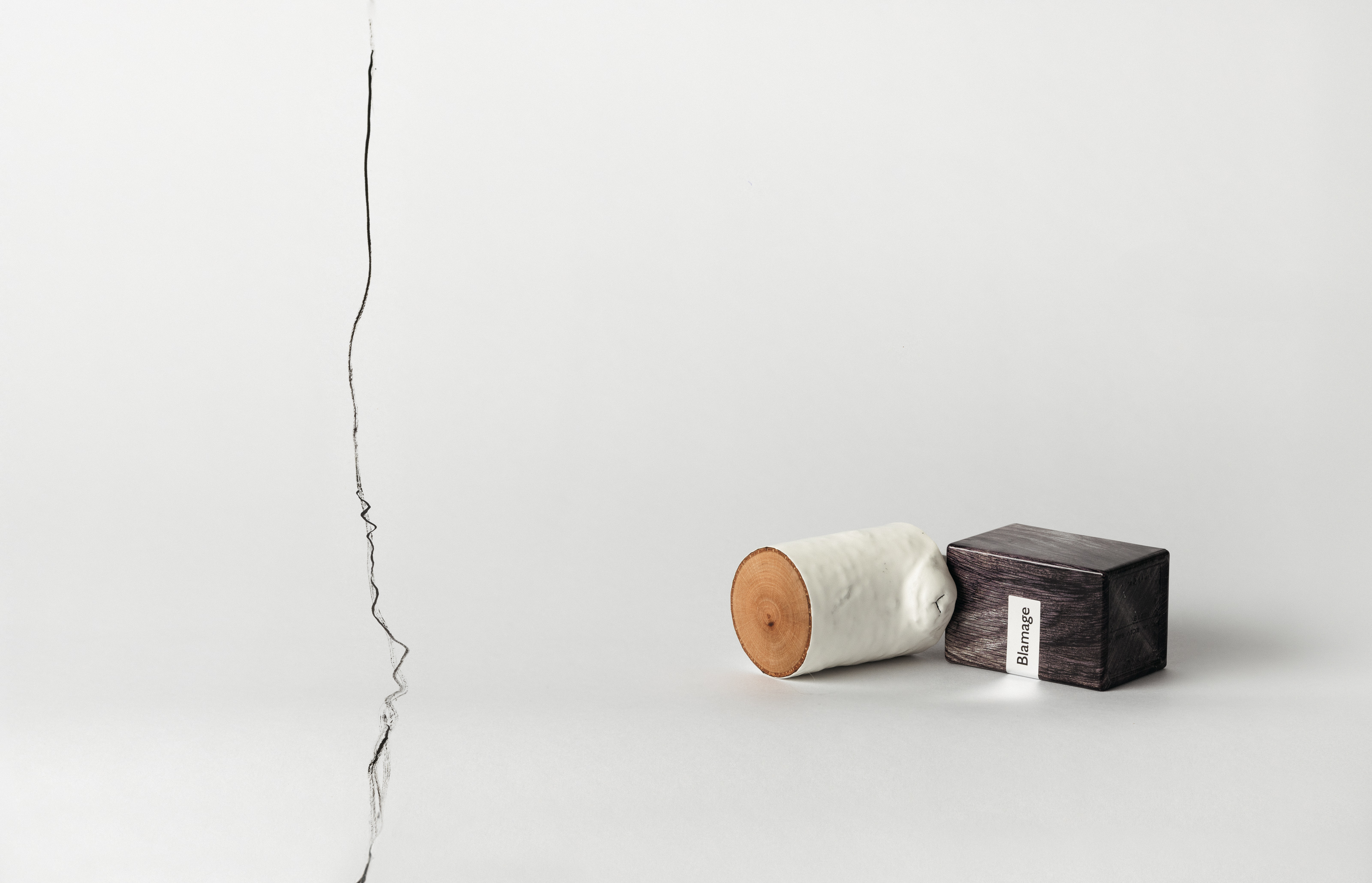 Nasomatto Blamage perfume bottle and its detached cylindrical cap lying on a pale surface beside an irregular dark line.