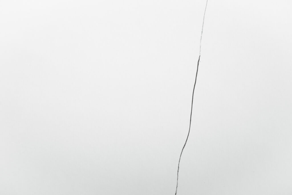 A single thin, irregular dark line extending vertically through an otherwise empty pale background.