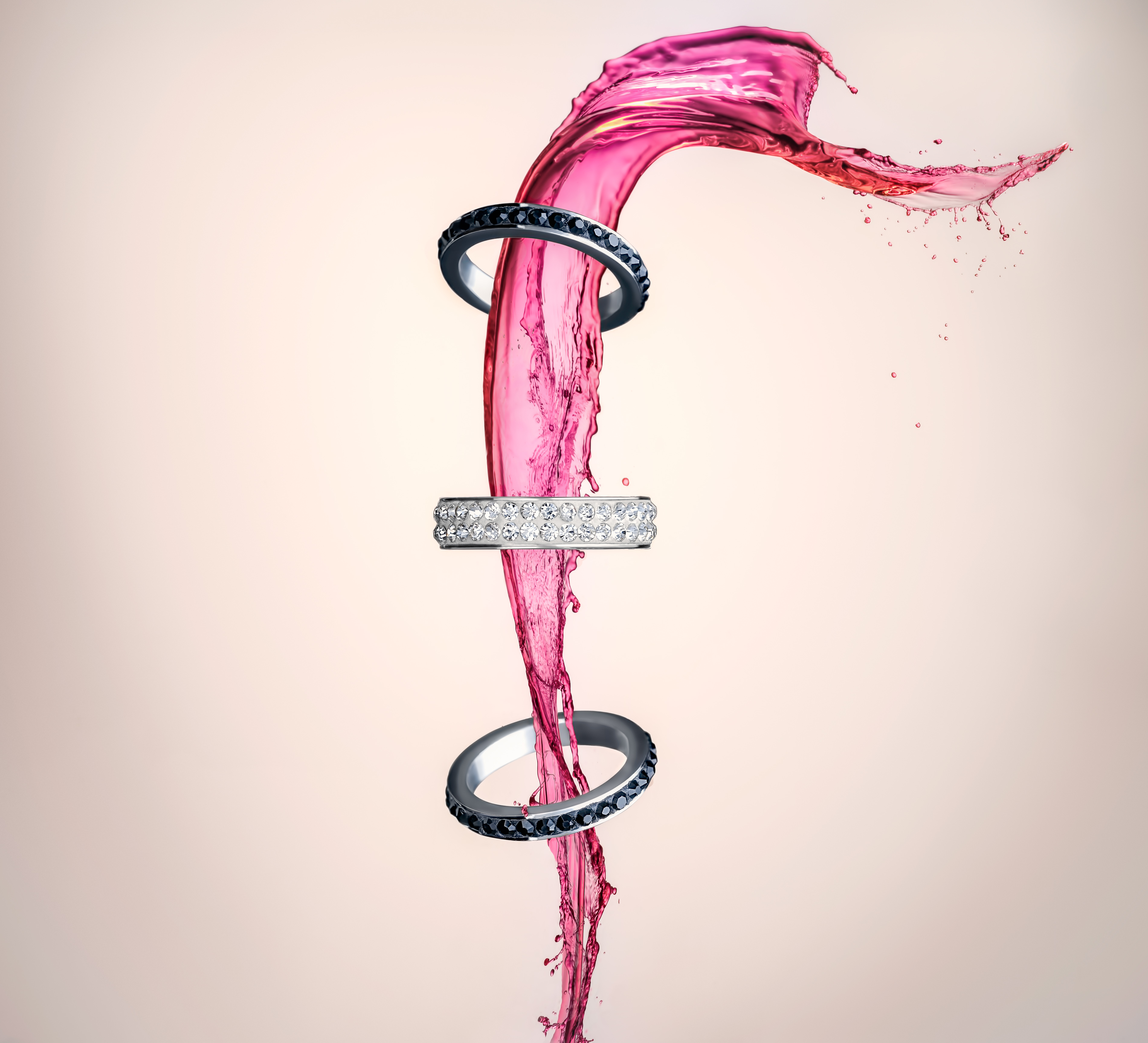Rings surrounded by a vivid magenta liquid splash in a creative still-life composition.