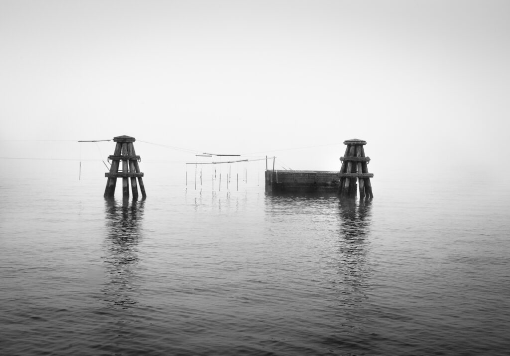 Weathered wooden mooring structures emerging from still water, surrounded by dense mist.