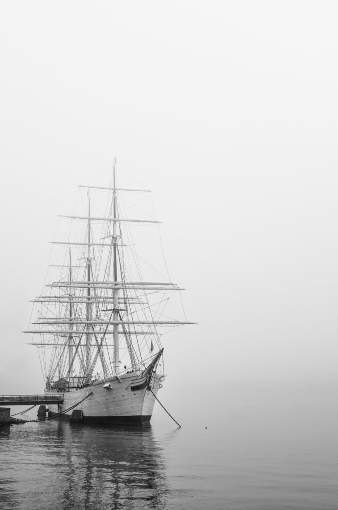 Historic sailing ship moored along the waterfront, its masts and rigging gradually disappearing into the mist.
