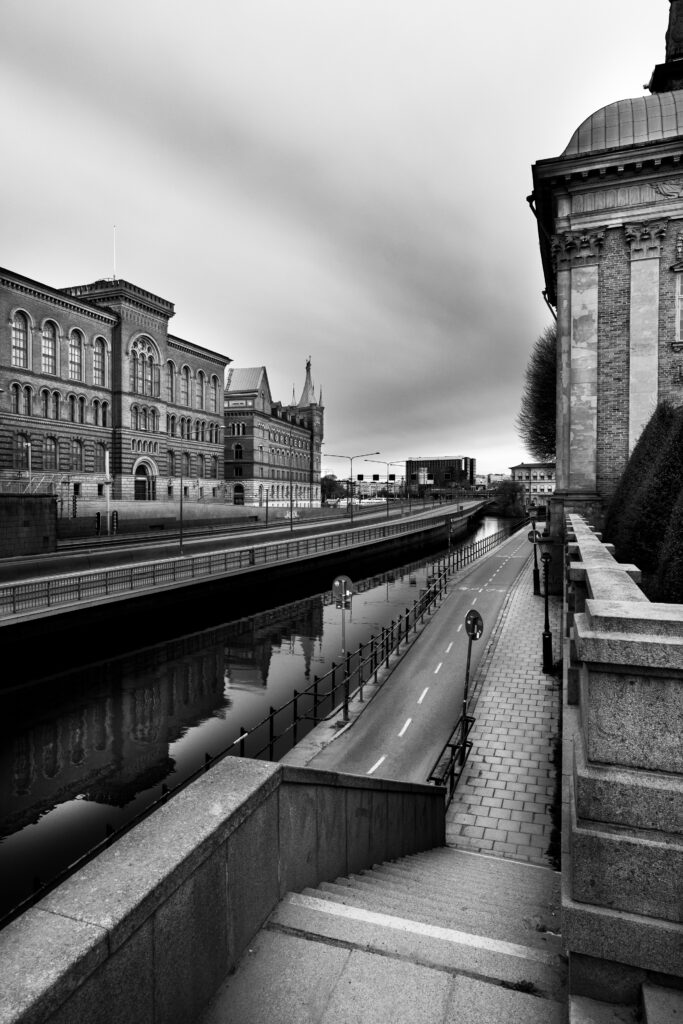 Stone steps descending beside a canal lined with historic buildings, photographed in black and white.